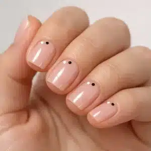 Manicura minimalista en uñas cortas con esmalte nude rosado translúcido, acabado gel ultra brillante y pequeños puntos decorativos en blanco y negro, fotografía macro profesional.