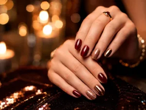 Uñas para fiesta en tonos rojo vino, dorado metálico y glitter con acabado brillante.